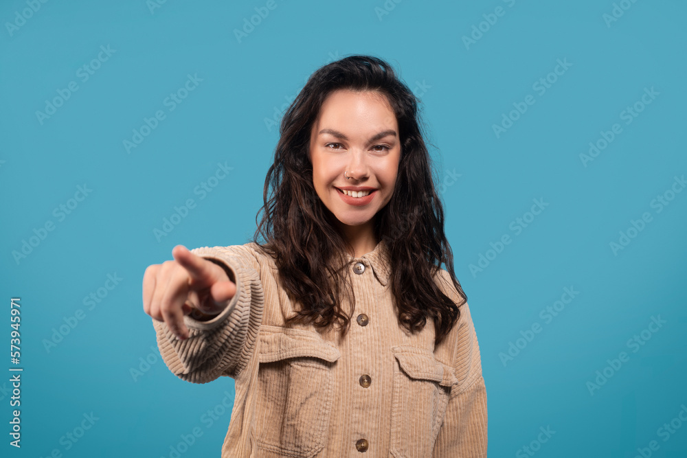 Cheerful millennial european woman student pointing finger at camera, isolated on blue background, studio