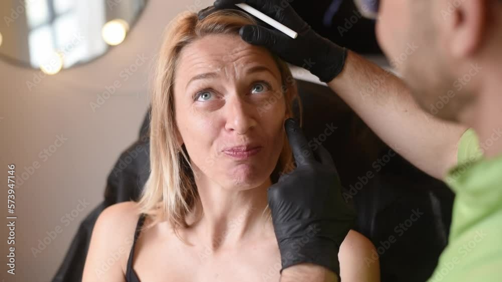 Man's hands in black gloves hold pencil and show on woman's face places for cosmetic injections. Make botox and hyaluronic acid in beauty salon against wrinkles on forehead