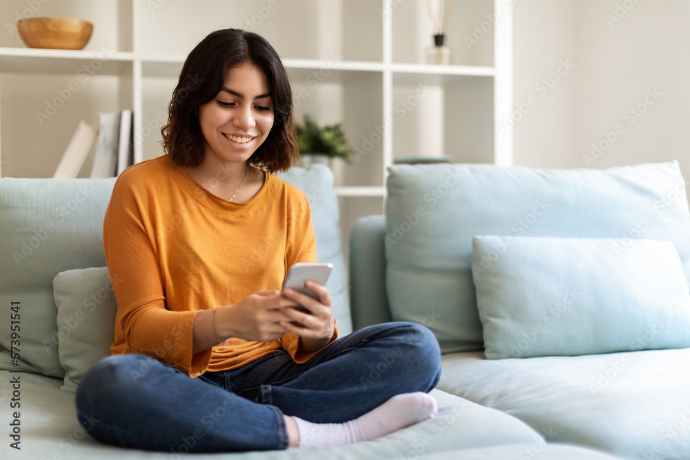 Smiling Young Arab Woman Resting With Smartphone On Couch At Home