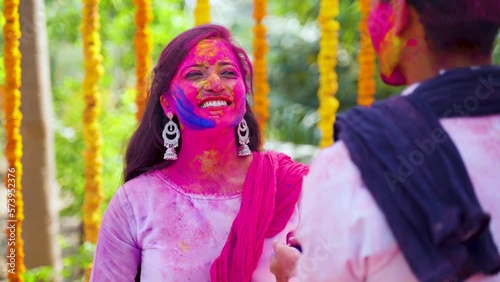 Shoulder shot of young man applying holi colors to girlfriend during holi festival celebrating on flower decoration background - concept of entertainment, relationships and enjoyment.