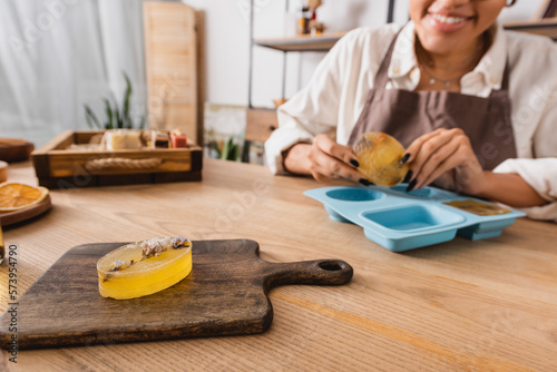 selective focus of herbal soap on chopping near cropped african american woman and silicone mold on blurred background.