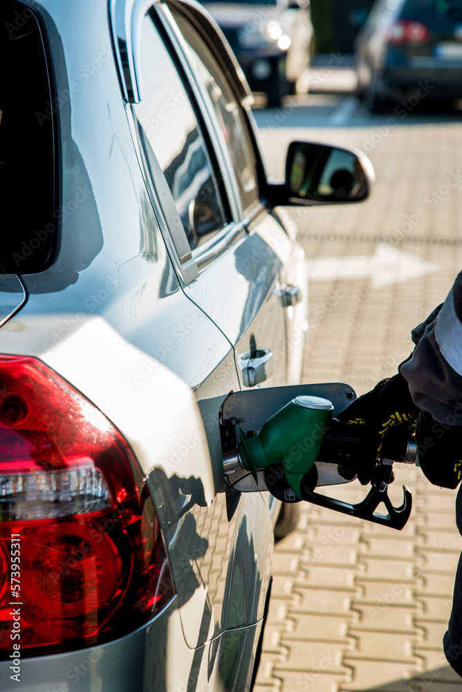 A man refueling a car at a gas station with a hose from an oil column inserted in the tank on a sunny day.