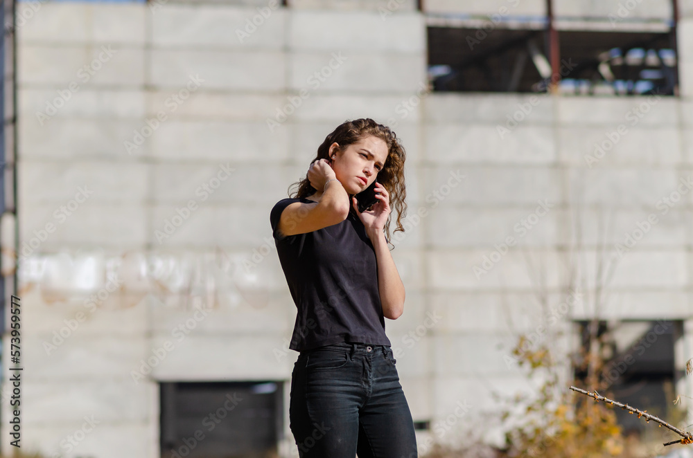 Sexy curly woman is talking on a mobile phone. Black T-shirt and jeans. Blurred background.