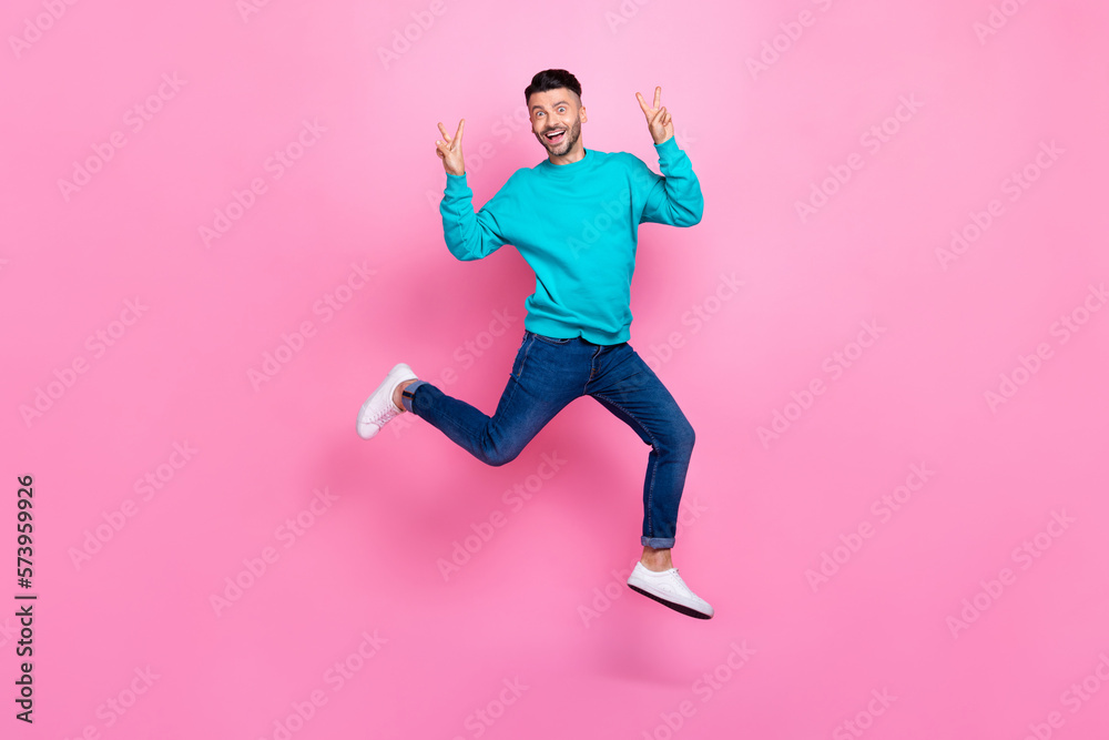 Full body photo of young nice guy jumping excited showing double v-sign dressed stylish blue clothes isolated on pink color background