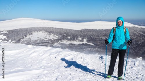 hiker girl stands in mountain glade admiring panorama of snowy mountains with frozen vegetation
