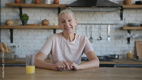 Healthy elderly woman in pink t-shirt sitting at the table with orange juice and looking at the camera