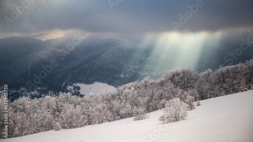 panorama of amazing idyllic landscape of the mountains during the cold winter; frosted bushes and sunshine breaking through the snowy clouds