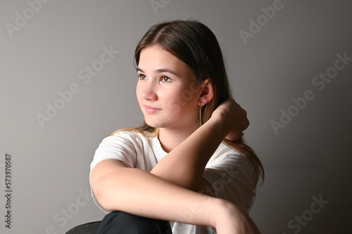 Portrait of a young beautiful thoughtful teen model in white t-shirt on gray background
