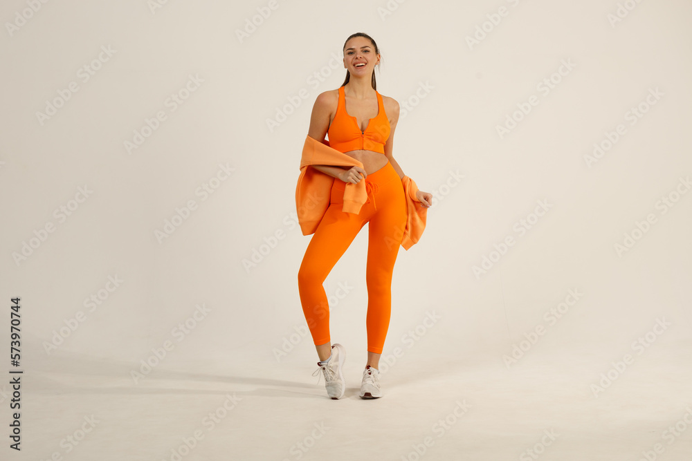 Obraz premium Young positive smiling girl in orange fitness sport outfit cloth suit studio isolated shot.