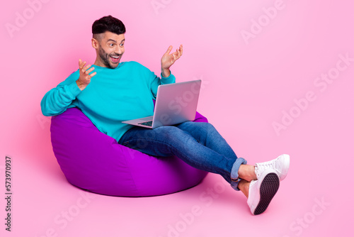Full length photo of young handsome man bean bag talk video conference netbook dressed stylish blue look isolated on pink color background