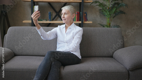Elderly successful business woman sitting on the sofa and talking on video call using smartphone
