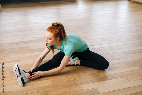 High-angle view of flexible fit woman practicing head to knee forward bend asana in yoga studio. Sport redhead female relaxing in deep stretching in Janu Sirsasana. Concept of healthy lifestyle.