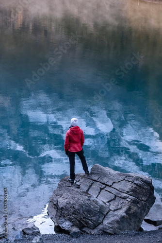 Sporty girl looking into reflection of mountains in lake. Lake Oeschinensee in Swiss alps. Travel, adventure, healthy lifestyle concept.