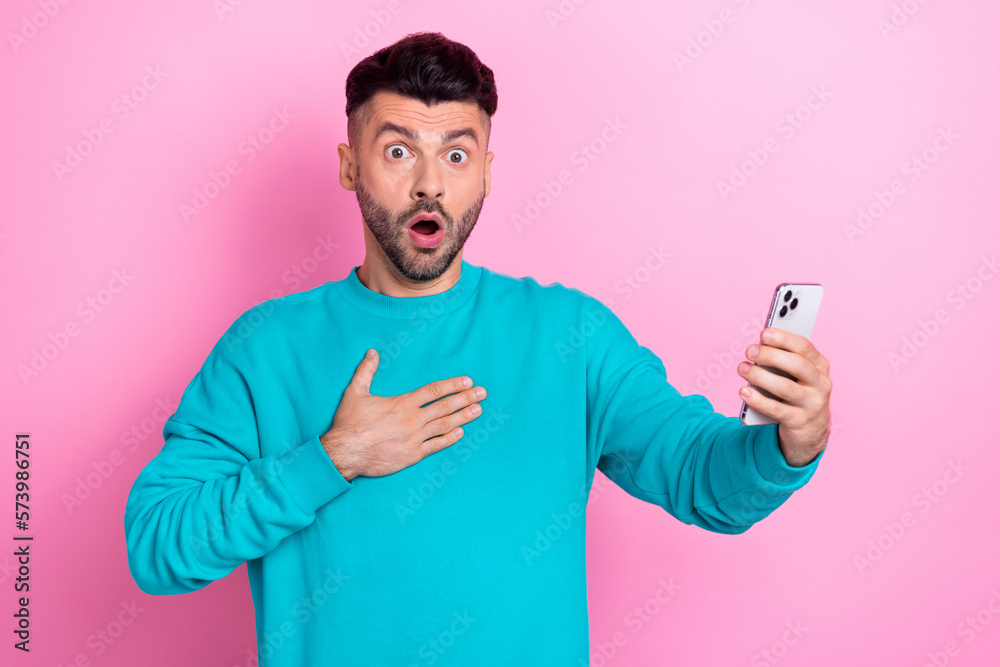 Portrait of shocked confused man arm touch chest open mouth hold telephone isolated on pink color background