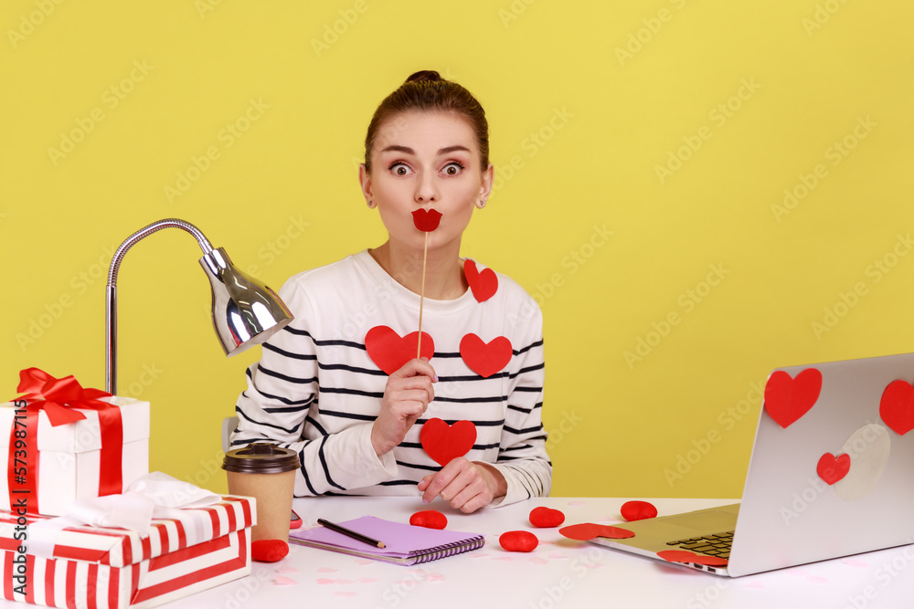 Woman sitting on workplace covered with heart sticks, covering her mouth with paper lips. Woman sitting on workplace covered with heart sticks, covering her mouth with paper lips.
