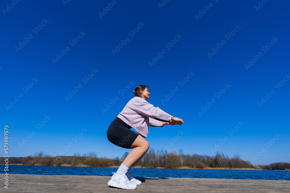 A young athletic woman squats during a workout.The shooting point from below. View of the pond A young athletic woman squats during a workout.The shooting point from below. View of the pond