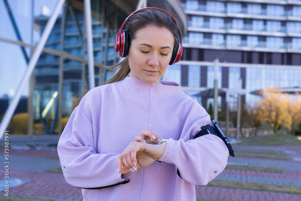 Fototapeta premium An athletic young woman adjusts her watch before running outside. Smart watches. A lover of running