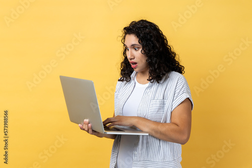 Shocked astonished woman working on laptop, looking at screen with big eyes and open mouth. © khosrork