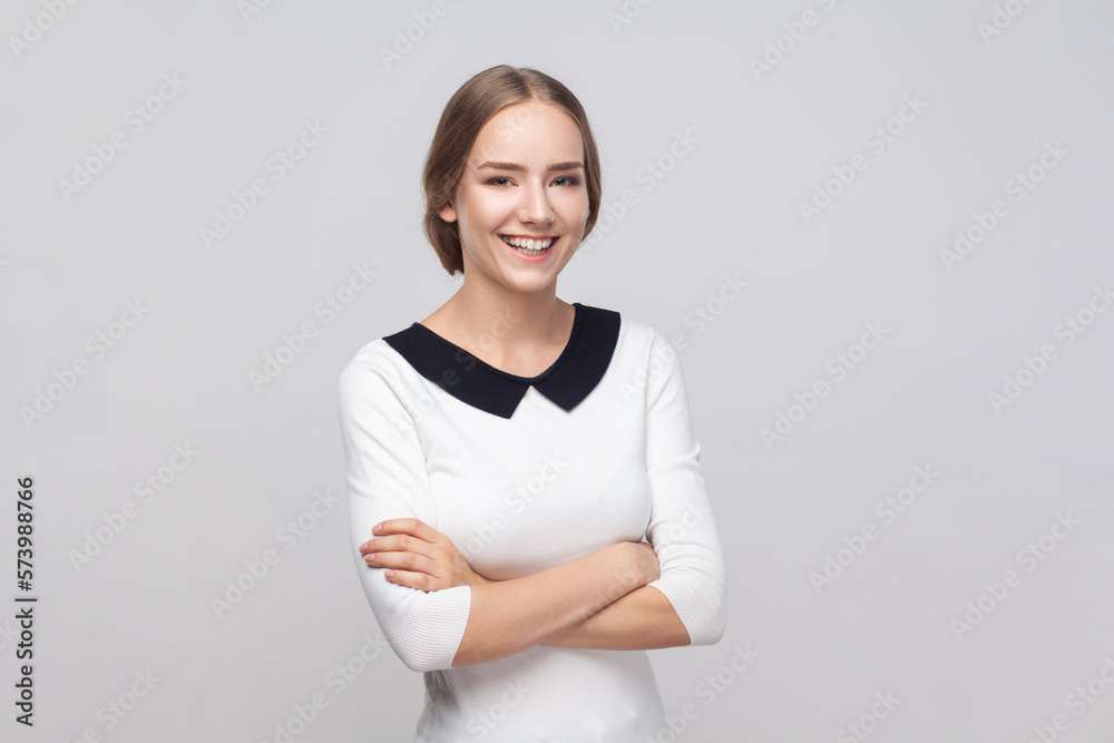Woman standing with crossed arms, looking at camera with toothy smile, expressing positive emotions. Woman standing with crossed arms, looking at camera with toothy smile, expressing positive emotions.