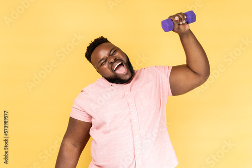 Man standing and raised arm with dumbbell, making effort raising heavy sport equipment.