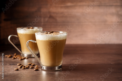 Two cups of coffee hot drinks, with milk foam in glass cups, over wooden background, copy space