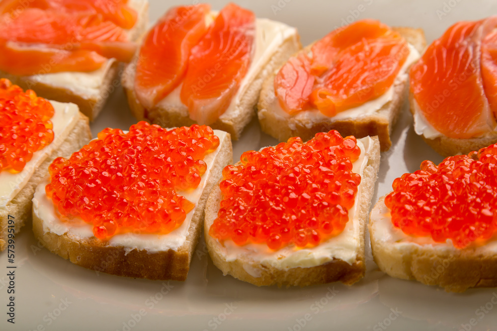 Toasts with red caviar and salted trout and butter on a plate close-up.