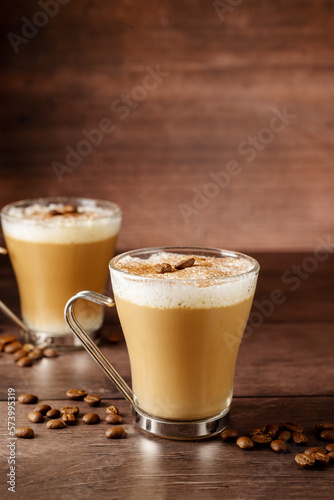 Two cups of coffee hot drinks, with milk foam in glass cups, over wooden background