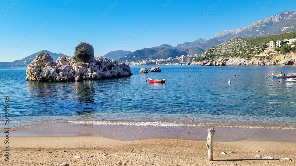 Floating fishermen boat with scenic view on small island with stone ruin near coastal village of Milocer near near Sveti Stefan, Budva Riviera, Adriatic Mediterranean Sea, Montenegro, Europe. Summer