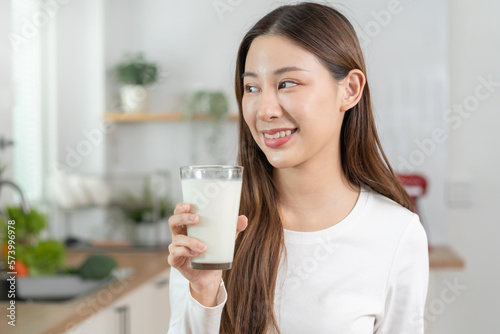 Health care, pretty asian young woman, girl drinking a glass of white fresh, dairy milk for calcium, vitamin wholesome good nutrition in morning at kitchen home. lifestyle, product healthy people.