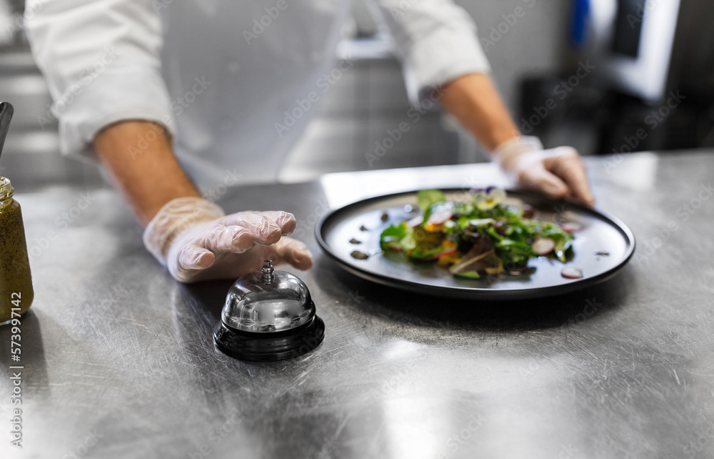 food cooking, profession and people concept - close up of male chef with plate of salad ringing bell at restaurant kitchen table