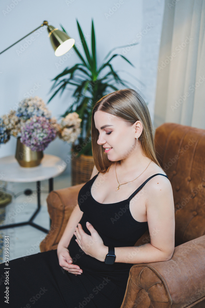 Attractive young blonde woman in black top and skirt sitting in brown chair and posing. Elegant woman in a soft chair. Attractive young blonde woman in black top and skirt sitting in brown chair and posing. Elegant woman in a soft chair.