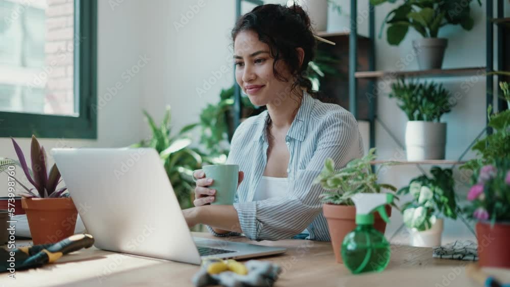 Video of smiling woman drinking a cup of coffee while working with her laptop in greenhouse. Video of smiling woman drinking a cup of coffee while working with her laptop in greenhouse.