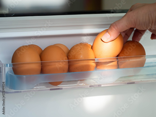 Eggs in the refrigerator. Close-up of a woman's hand holding an egg with light and shodow photo