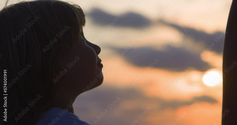 Close-up back of head of boy with blonde hair who looks up at his mom with love and respect and holds her hand. Child and his mother on background of beautiful orange sunset hold each other hands. Close-up back of head of boy with blonde hair who looks up at his mom with love and respect and holds her hand. Child and his mother on background of beautiful orange sunset hold each other hands.