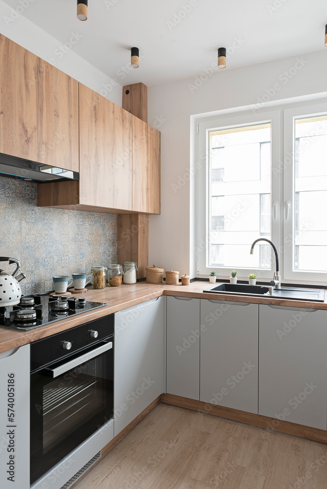 Fototapeta premium Interior of small kitchen with sink near window and wooden cabinets in kitchen furniture. Stove with gas and kettle. Counter top in the kitchen with stove and wooden floor.