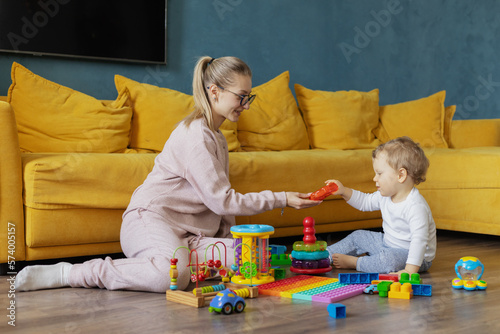 A young mother plays educational games with her baby at home on the floor