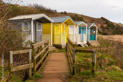 Coloured beach huts above a sandy beach with wooden boadwalk for access photo