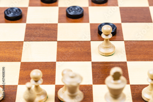 playing by different rules on the same board - black checkers and white chess figures on wooden chessboard  pawn and checkers piece moves closeup  focus on the pawn 