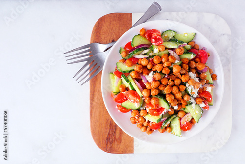 Healthy Mediterranean salad with chick peas. Overhead view on a serving platter over a white marble background.