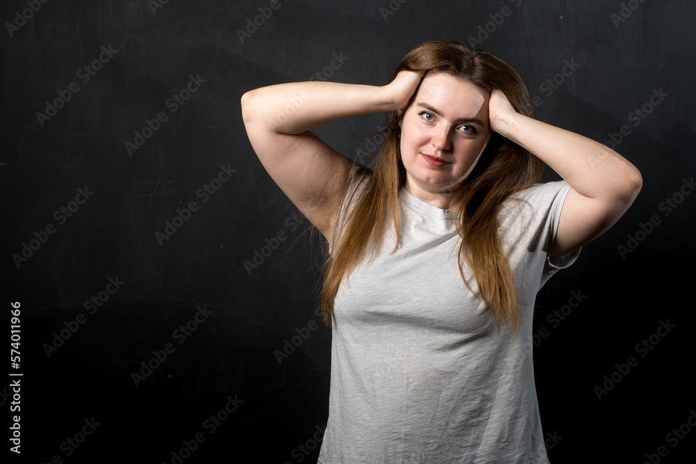 a girl of European appearance on a black background holds her head with her hands. stress and emotions. a girl of European appearance on a black background holds her head with her hands. stress and emotions.