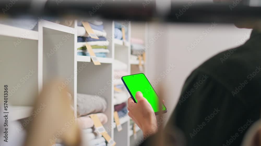 Closet for clothes, Young modern woman Focusedly Holds the phone looks into the green screen of smartphone. Stack of seasonal clothes, Concept Chooses a dress in a clothing warehouse, business woman
