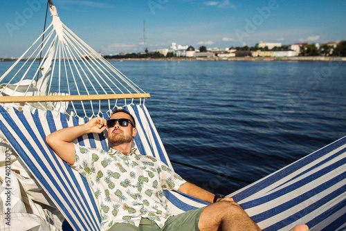 Handsome man rests in a hammock on a yacht. Leisure and fun in a water