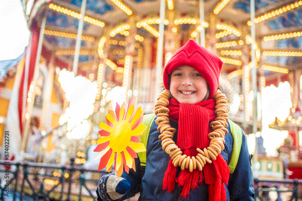 Obraz premium smiling boy with bagel beads, at the traditional Russian festival dedicated to the meeting of spring, the week of pancakes, Shrovetide. the child stands at the decorations for the Maslenitsa holiday