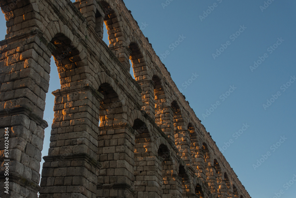 Roman aqueduct in stone with its arches illuminated by the evening light and isolated against the blue sky