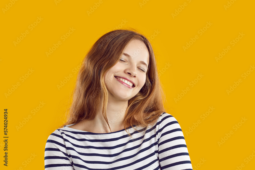 Human emotions. Portrait of happy young woman with closed eyes and dreamy and satisfied expression on her face. Close up of cute Caucasian girl in casual clothes smiling on orange background. Human emotions. Portrait of happy young woman with closed eyes and dreamy and satisfied expression on her face. Close up of cute Caucasian girl in casual clothes smiling on orange background.
