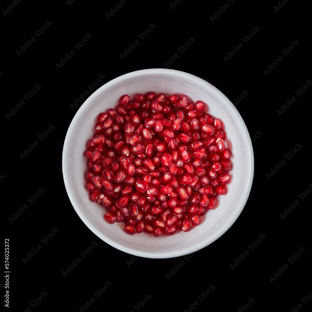 white plate with pomegranate seeds on a black background. white plate with pomegranate seeds on a black background.