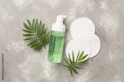 Foaming facial cleanser and with eco pads on concrete background, top view