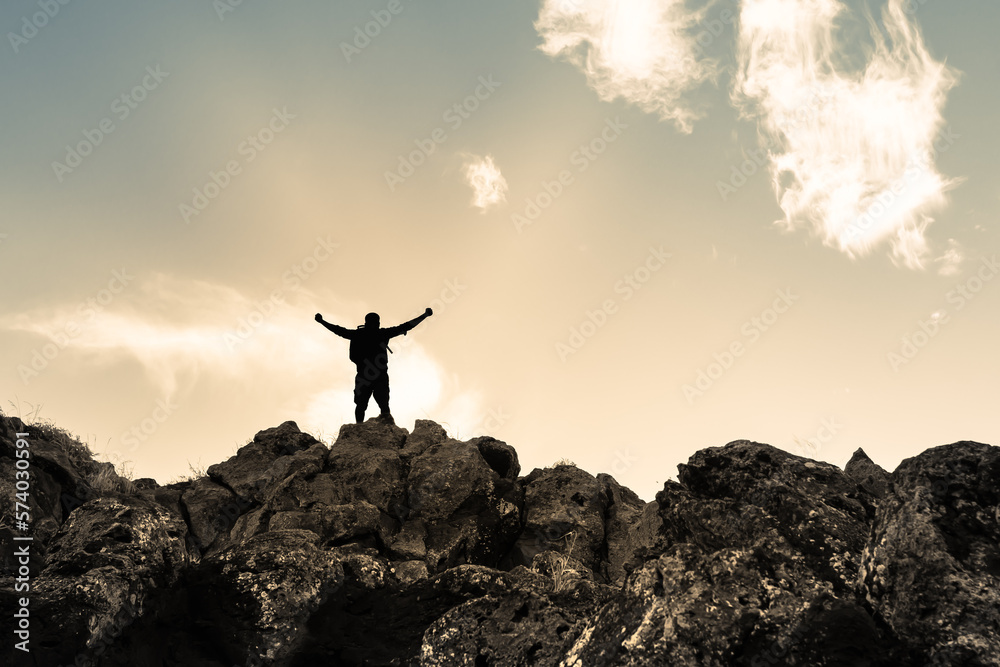 Victorious man on a mountain with arms raised in the air. 