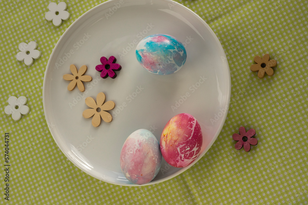 Colorful Easter pink red and light blue batik eggs on the table with flower decorations around, handmade homemade diy crafts