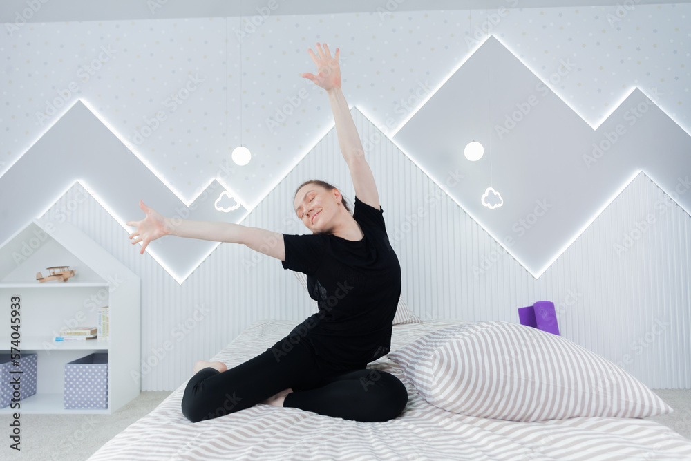 Young woman practicing yoga, working out, wearing sportswear, black top and pants, indoor full length, clear bright background. Sport and healthy active lifestyle concept.